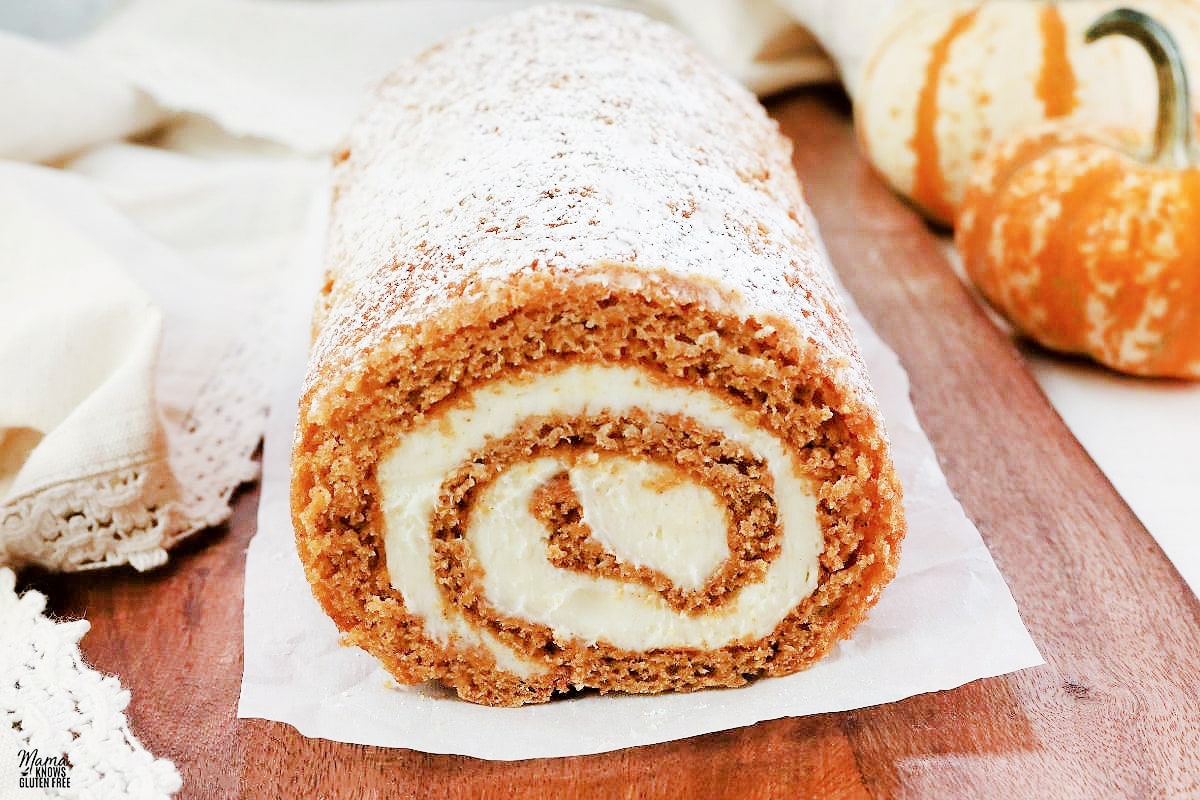 gluten-free pumpkin roll on a wood cutting board with pumpkins in the background