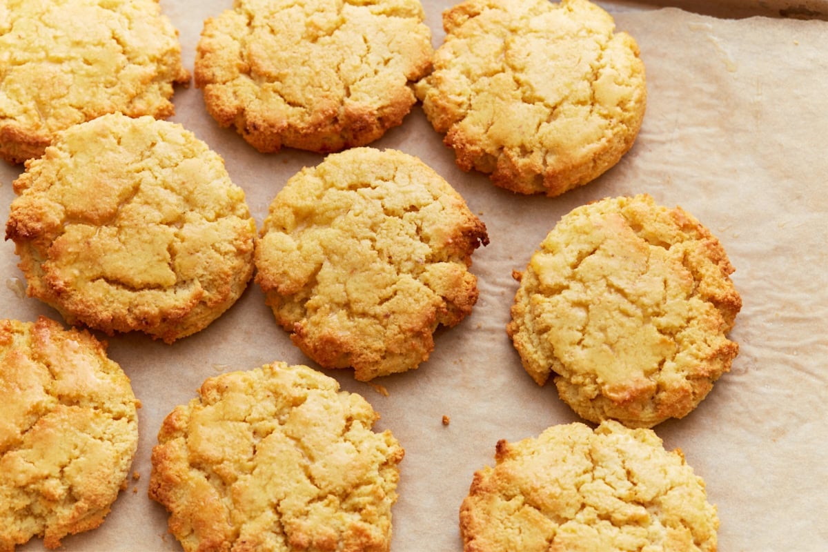 Top-down view of freshly baked almond flour biscuits on a parchment-lined baking sheet, showcasing their golden brown, slightly craggy tops and crisp edges.
