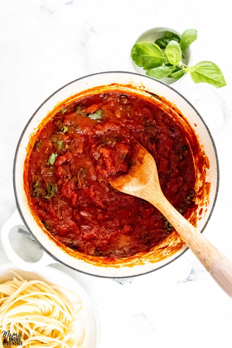 gluten-free spaghetti sauce in a white pot with cooked spaghetti pasta and basil on the side