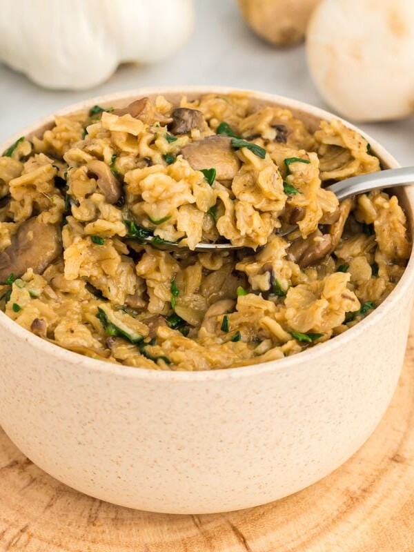 Savory oatmeal in a bowl with a spoon, with spinach, garlic and mushrooms in the background.