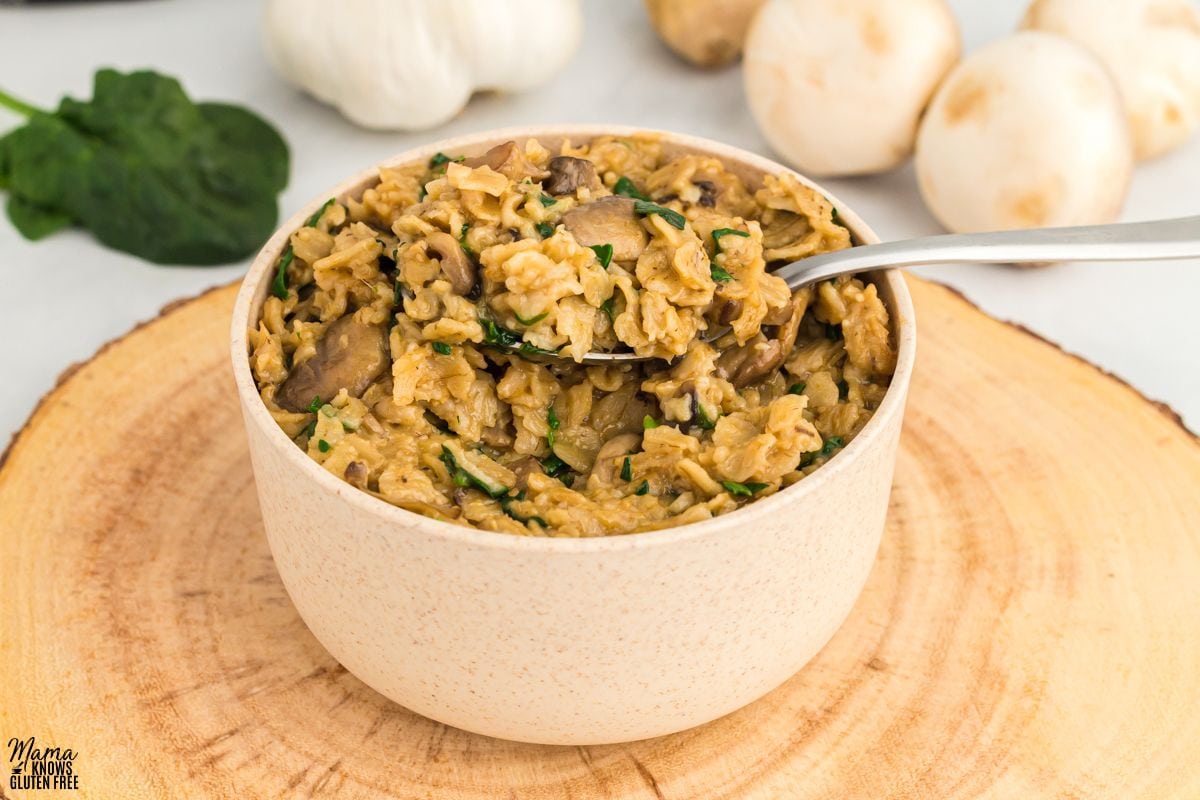 Savory oatmeal in a bowl with a spoon, with spinach, garlic and mushrooms in the background.