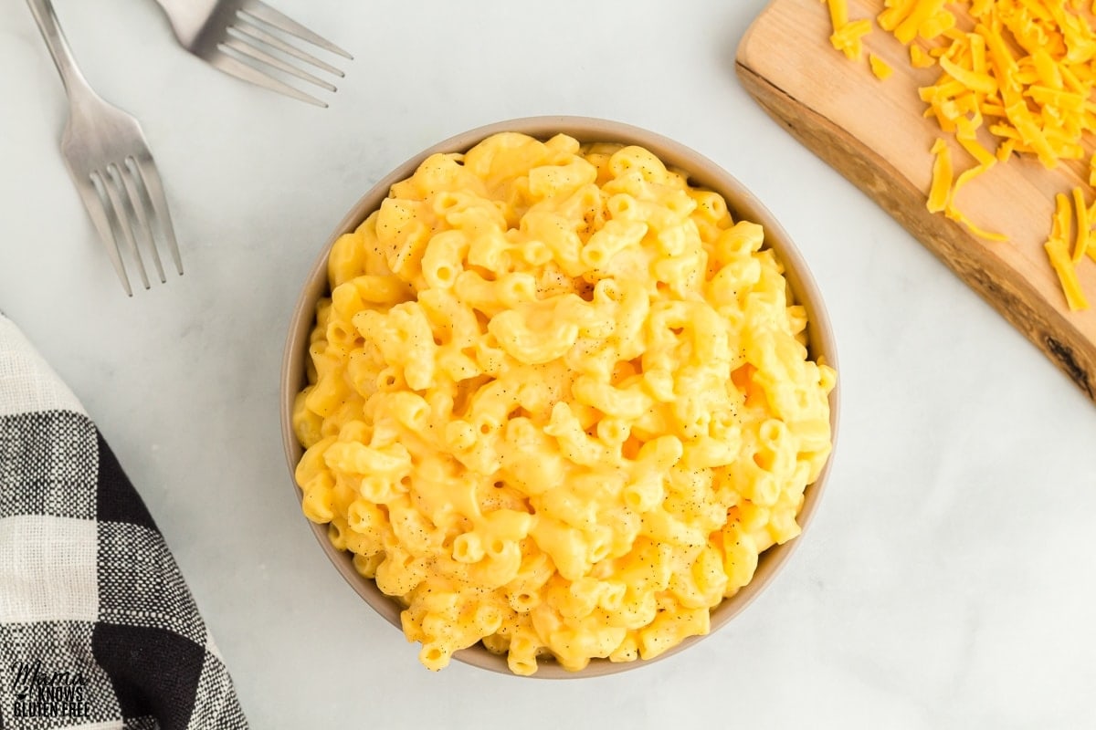 gluten-free mac and cheese ibn a bowl with forks, cutting board with cheese, and a napkin