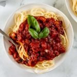 gluten-free spaghetti sauce over pasta in a white bowl topped with basil