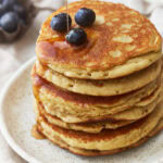 three-quarters view of a stack of almond flour pancakes on a plate with blueberries and syrup.