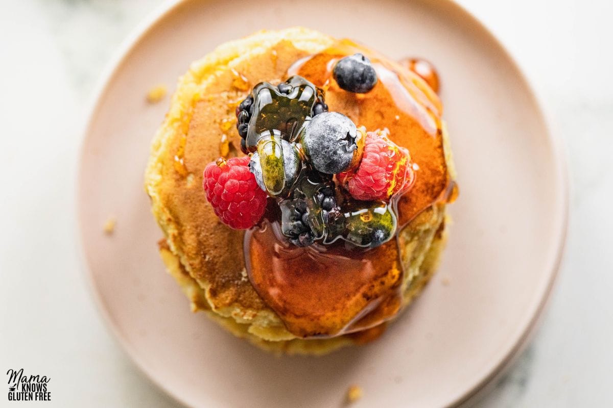 A stack of almond flour pancakes with berries and syrup, taken from above.