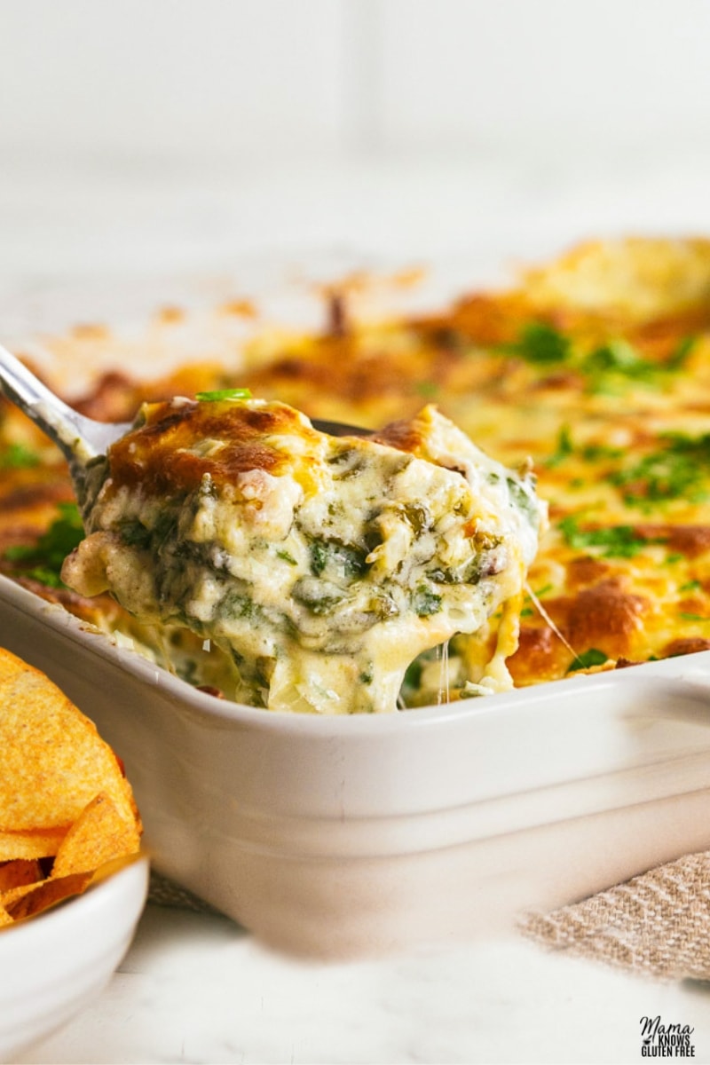 serving spoon filled with spinach dip with spinach dip in white baking dish