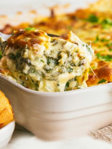 spinach dip in a white baking dish with a serving spoon