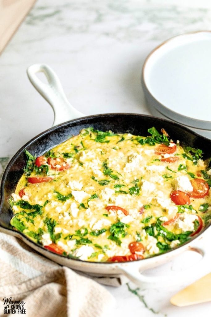 Frittata with tomatoes and spinach in a skillet. Some empty plates in the background.