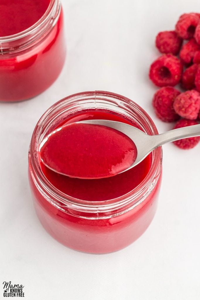 Raspberry coulis in a jar. A spoonful of coulis above the jar.