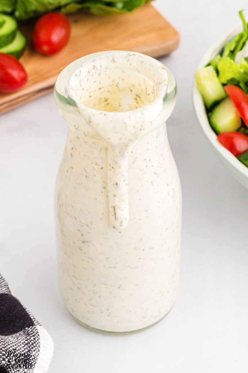 dairy-free ranch dressing poured out of a glass bottle with a salad in the background 