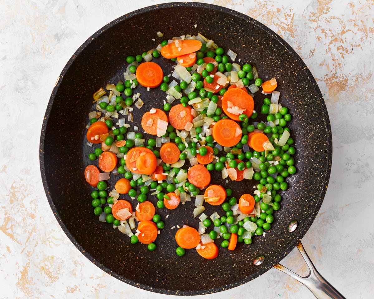 Frozen peas, carrots, and diced onion in a skillet