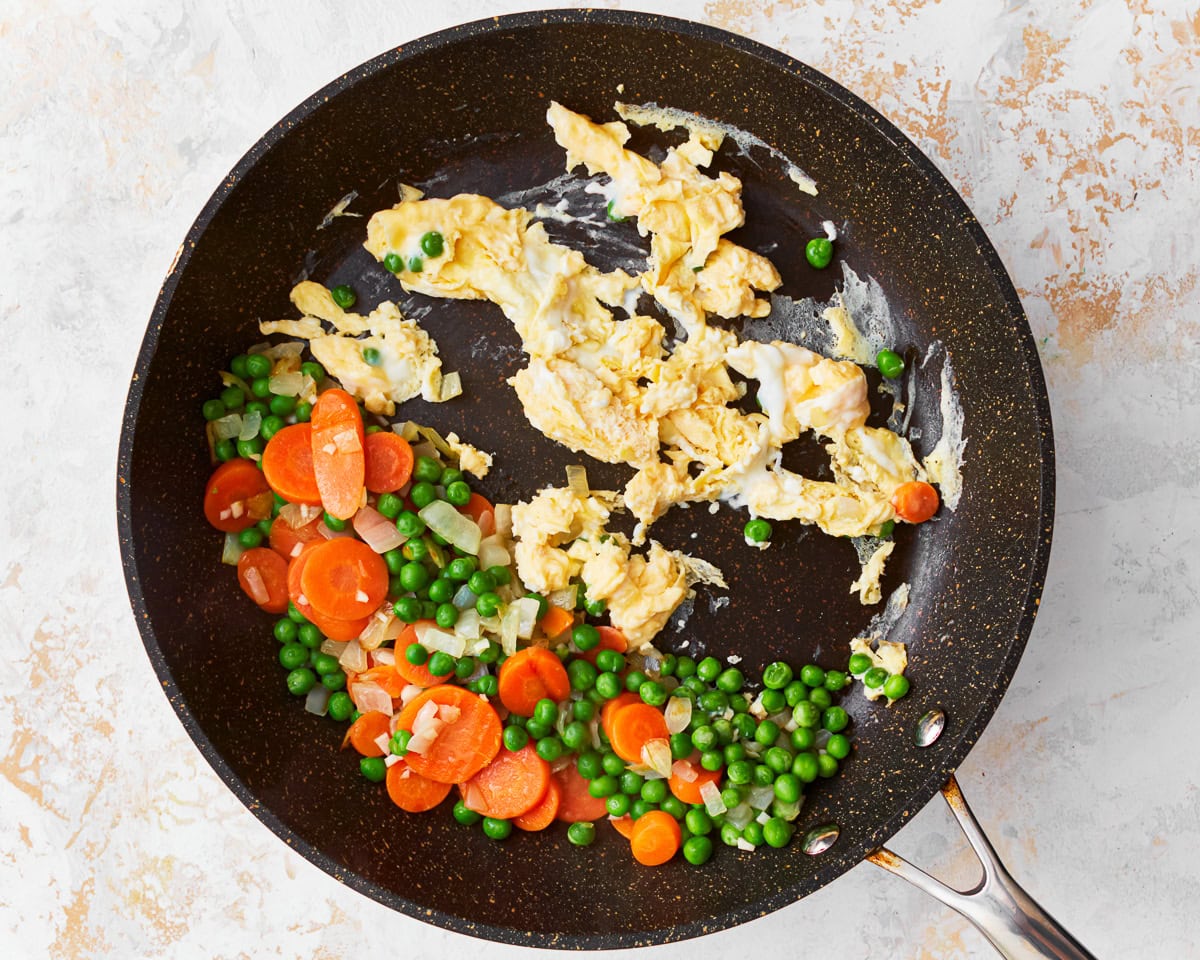Peas, carrots, and onion in a skillet with scrambled eggs