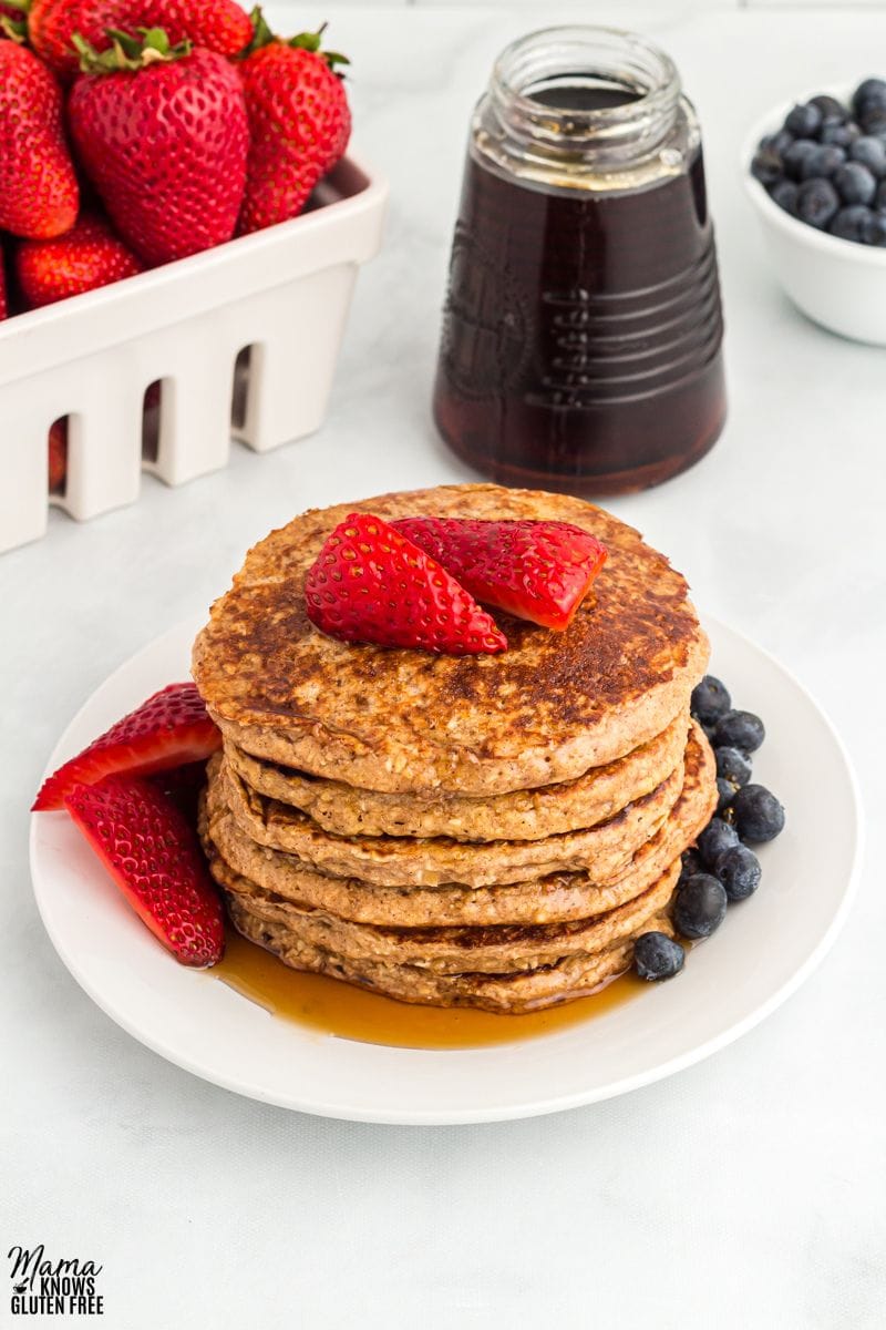 Oatmeal Pancakes on white plate topped with fresh strawberries, blueberries and maple syrip