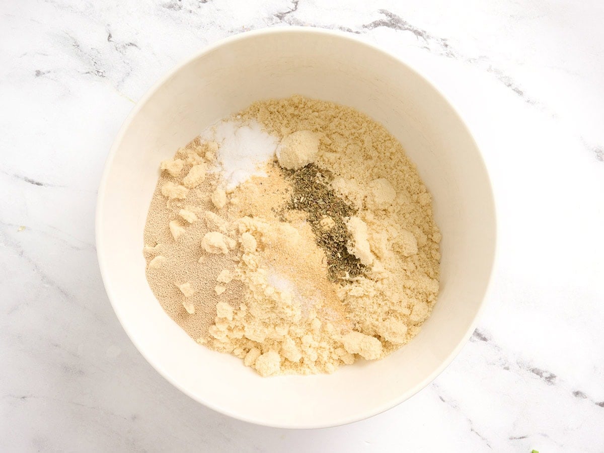 Almond flour, instant yeast, garlic powder, onion powder, dried basil, and salt in a white mixing bowl before combining