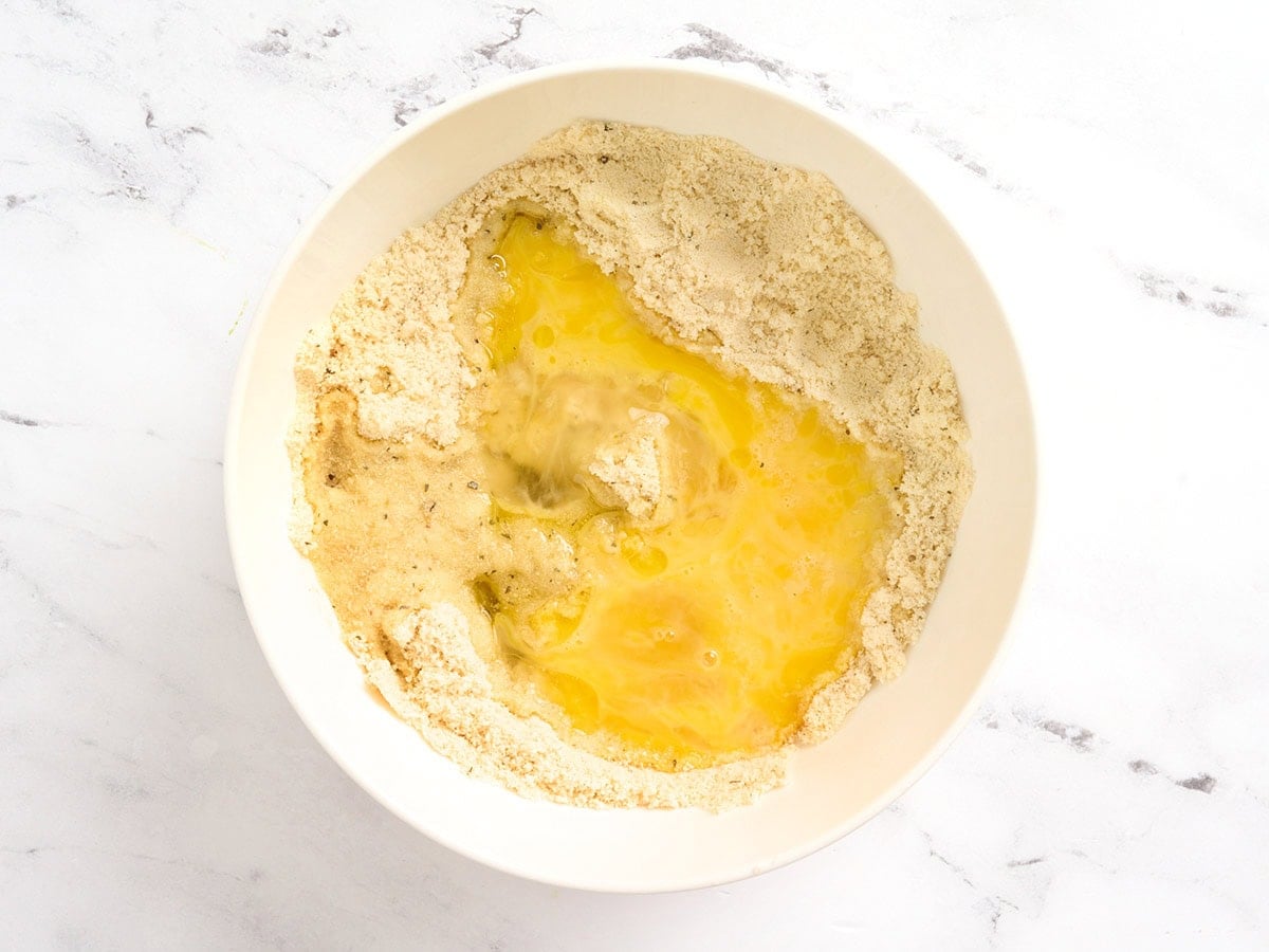 Whisked egg poured into a well in the almond flour mixture in a white mixing bowl