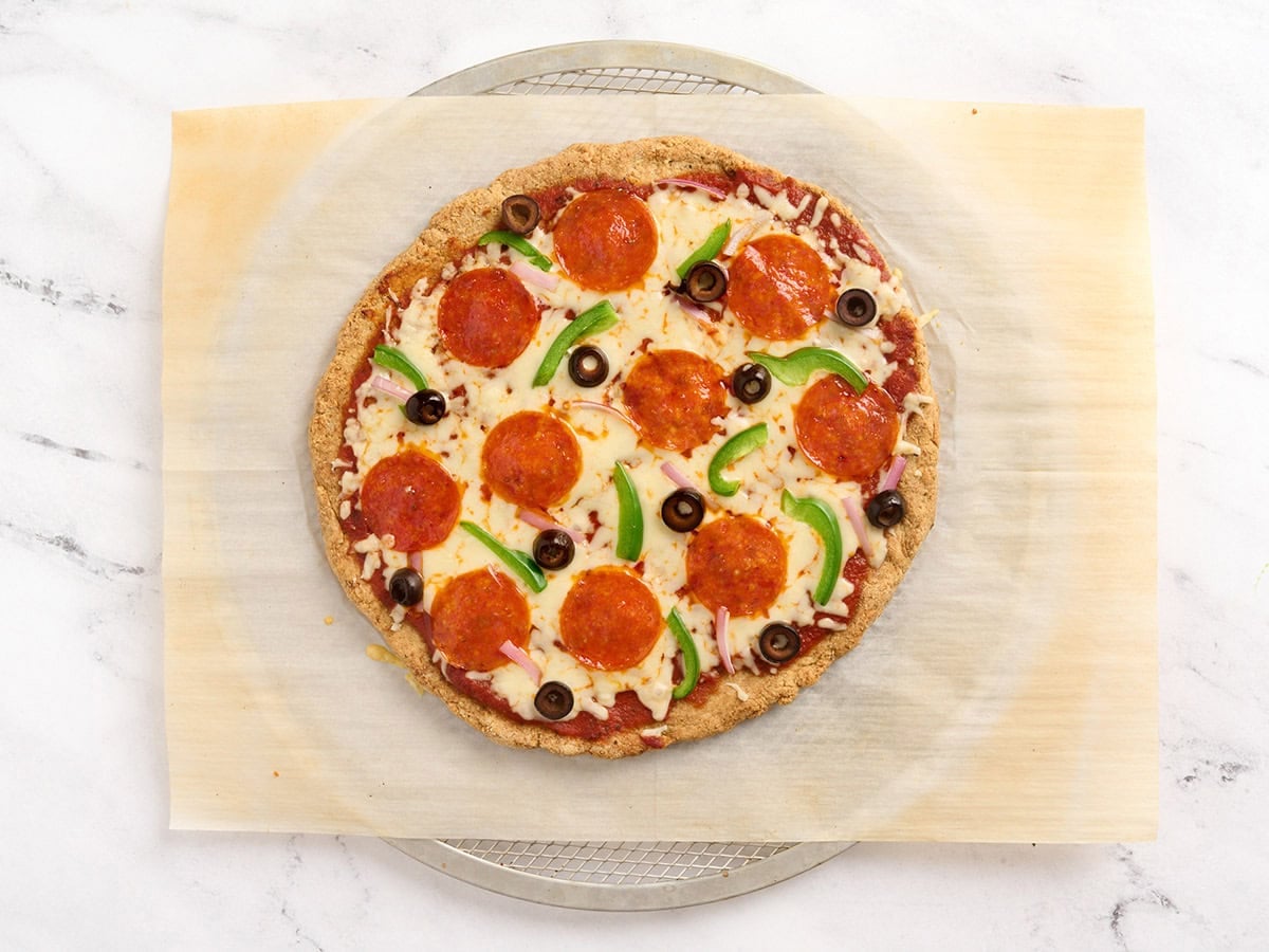 Baked almond flour pizza crust topped with sauce, melted cheese, pepperoni, black olives, green pepper, and red onion