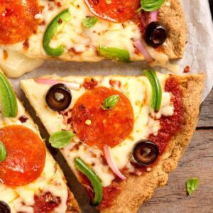 Close-up of almond flour pizza crust slices topped with pepperoni, black olives, green pepper, red onion, and fresh basil