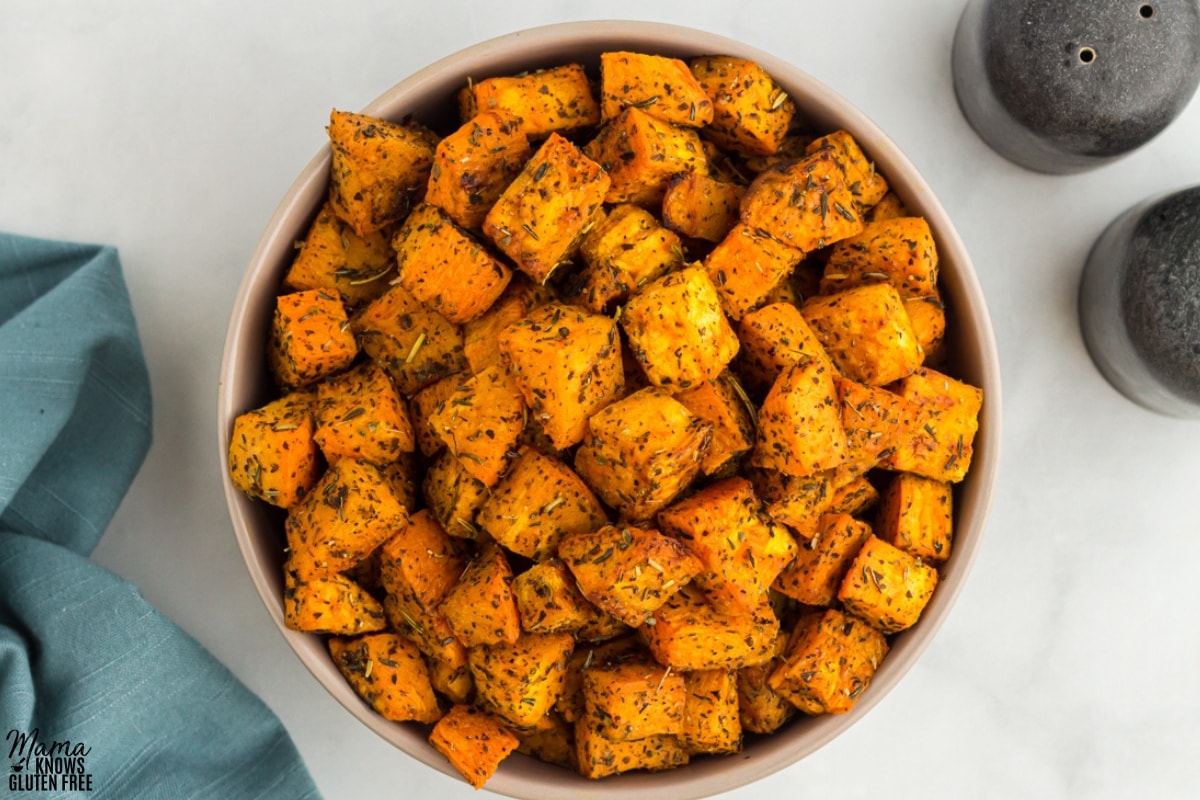 Roasted Sweet Potatoes cubes tossed in herbs and placed in bowl.