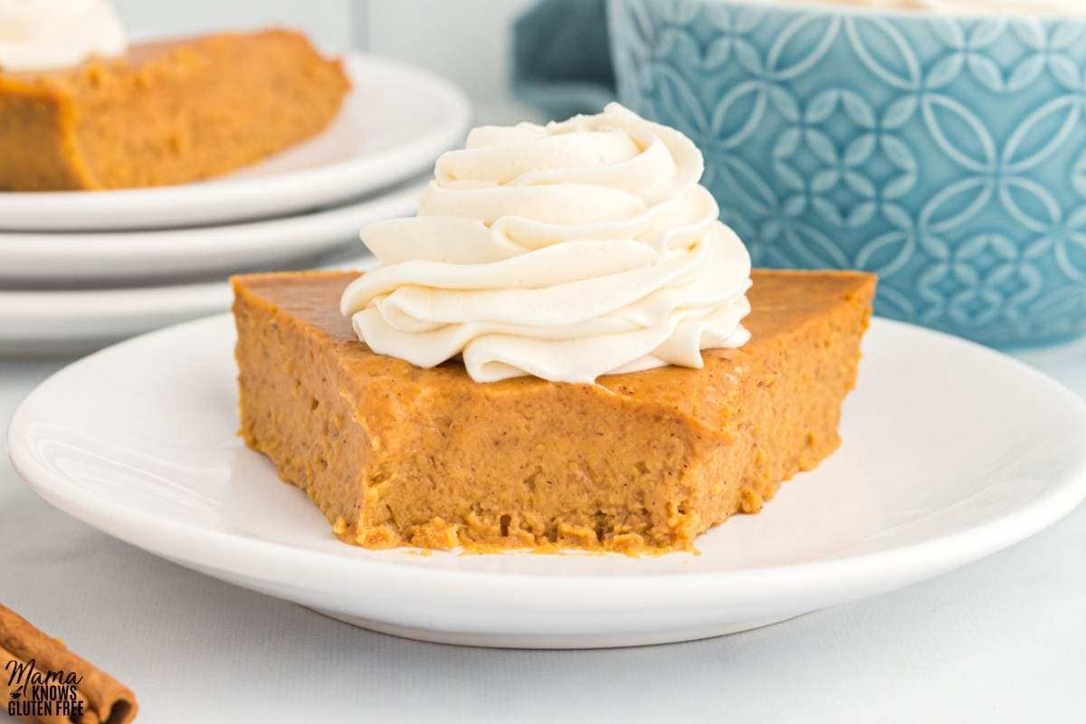 Slice of Gluten-Free Crustless Pumpkin Pie topped with whipped cream on white plate with a spoonful removed.