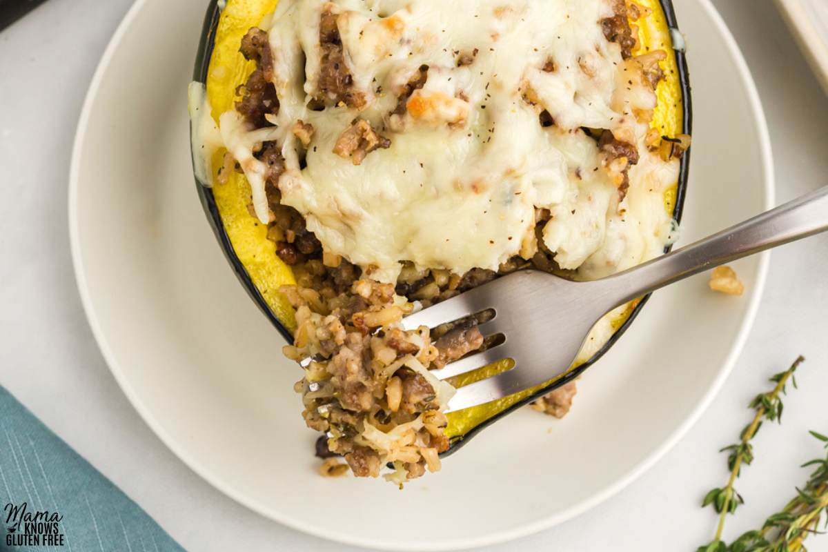 A fork scooping stuffing out of a single Gluten-Free Stuffed Acorn Squash on a white plate.
