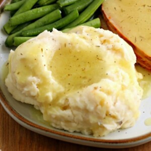 gluten-free gravy over mashed potatoes with turkey on green beans on a white plate.