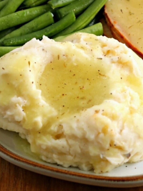 gluten-free gravy over mashed potatoes with turkey on green beans on a white plate.