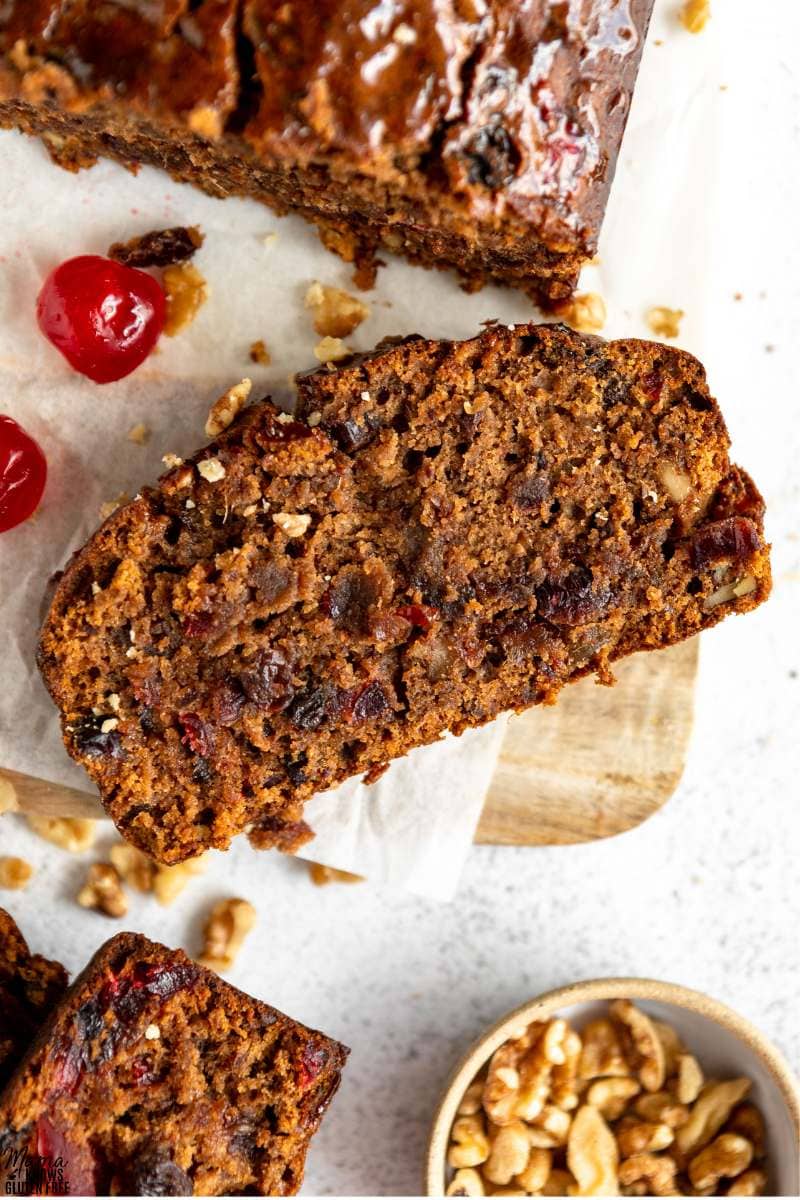 Overhead shot of a slice of Gluten-Free Fruit Cake on parchment paper and wooden board.