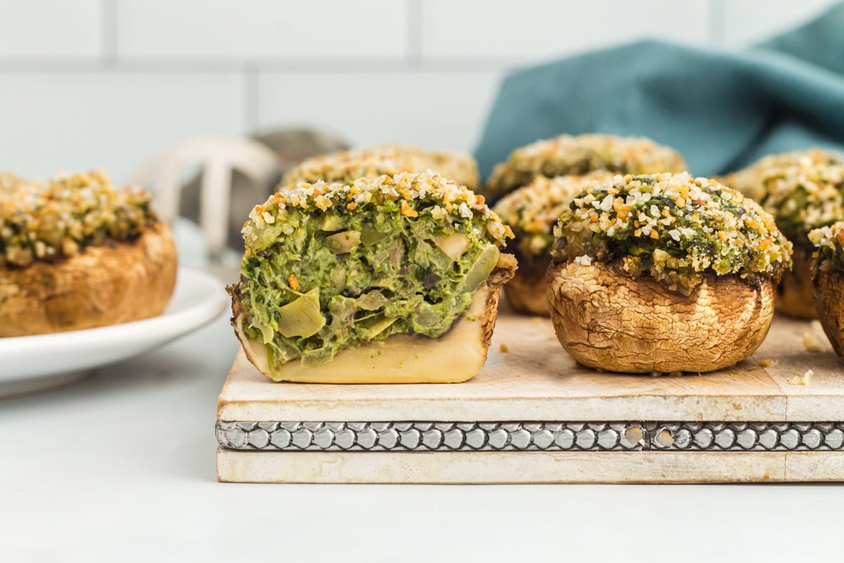 A gluten-free stuffed mushroom sliced in half on a chopping board with other stuffed mushrooms.