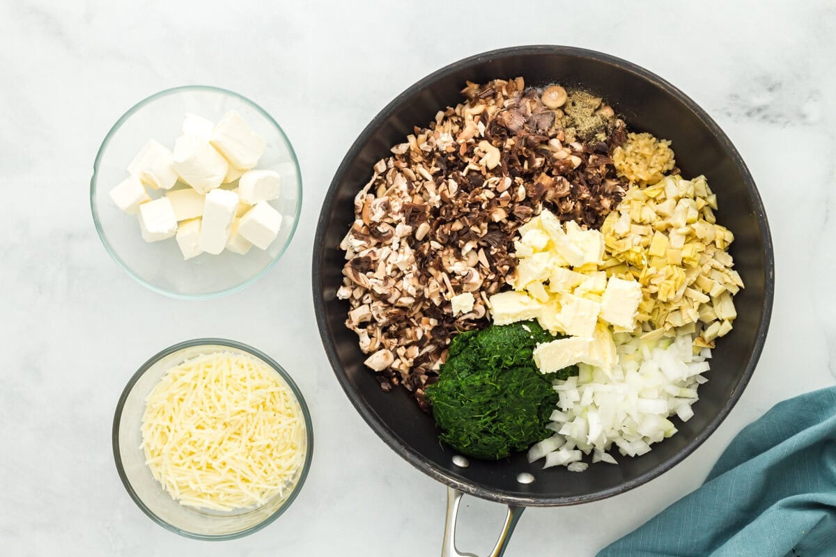 Chopped mushrooms, spinach, onions, and chopped artichoke hearts in a skillet.
