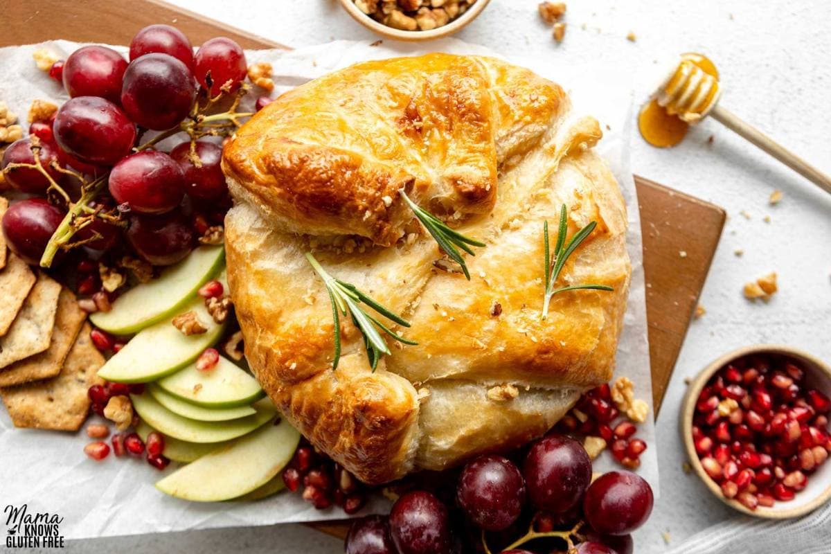 Gluten-Free Baked Brie surrounded by grapes, sliced apples, pomegranate seeds and crackers.
