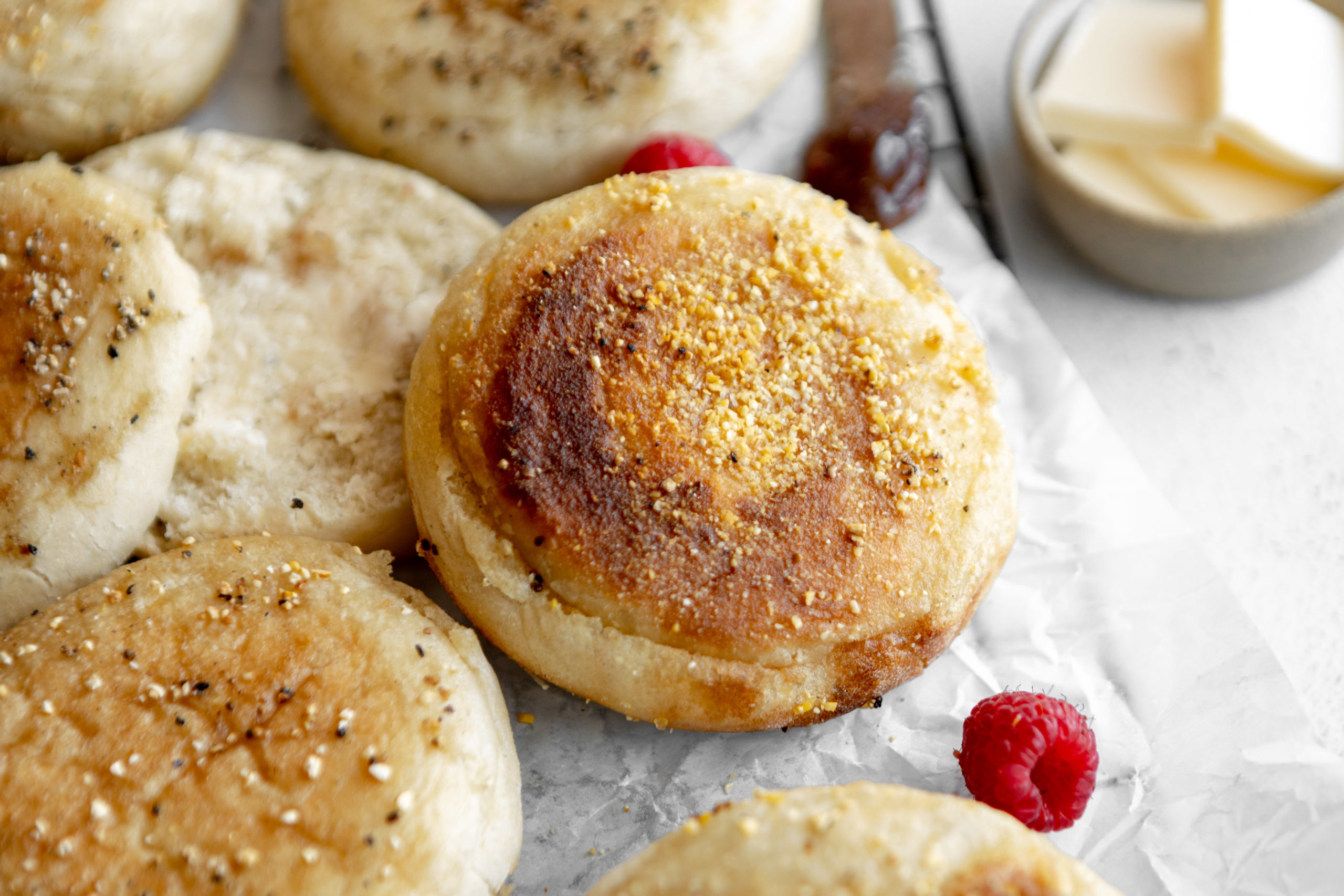 Gluten-free english muffins on parchment paper with raspberries.
