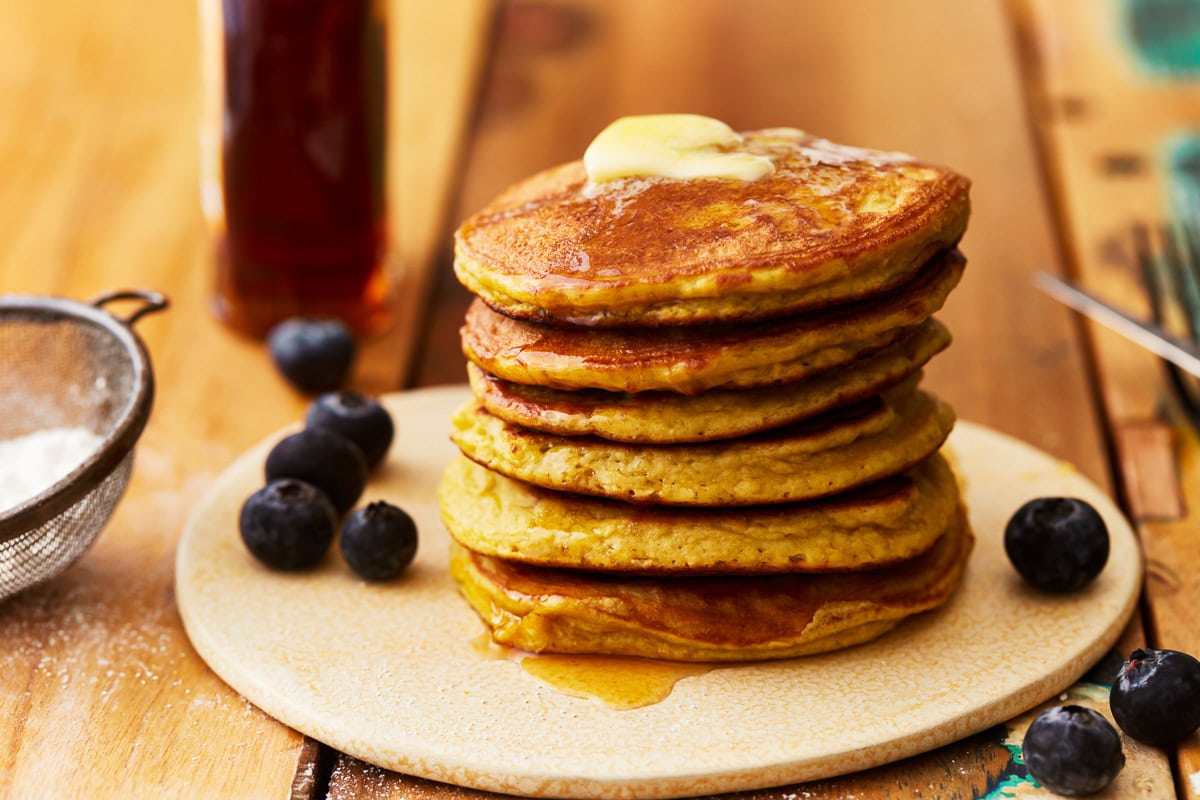 coconut flour pancakes stacked on a plate with butter and blueberries.