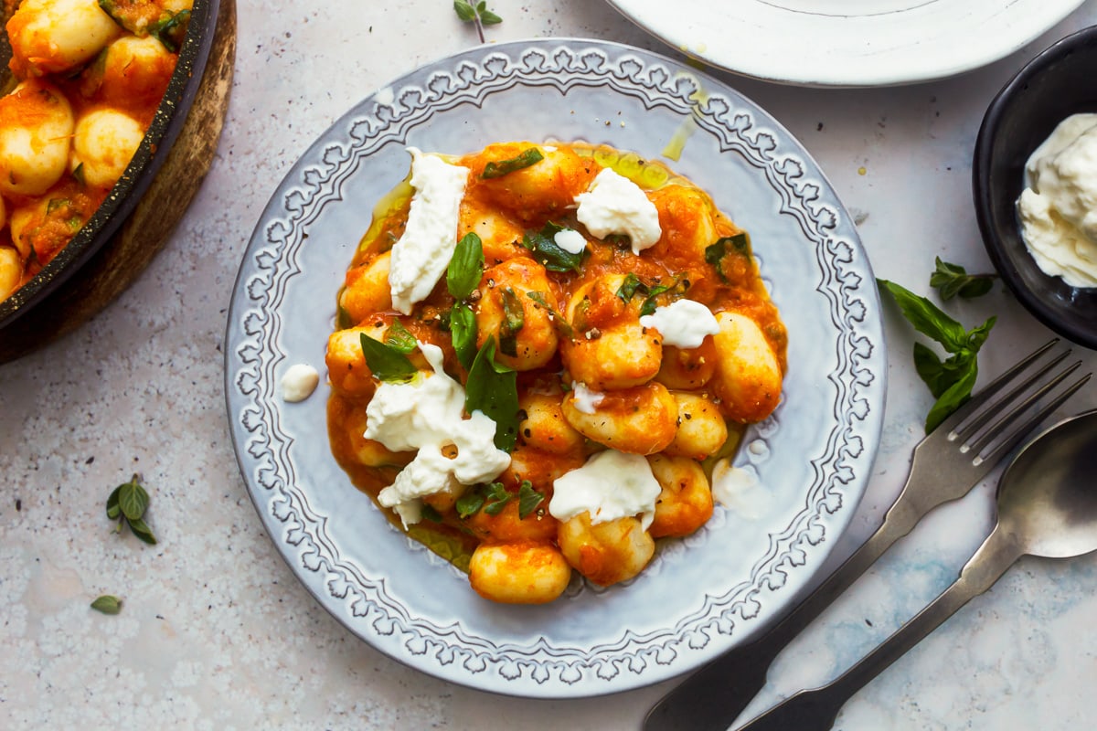 gluten-free gnocchi in tomato sauce in a white bowl topped with cheese and basil