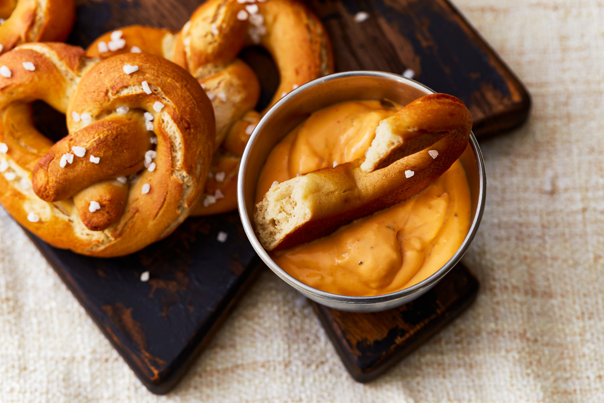 Piece of gluten-free soft pretzel dipped in mustard.
