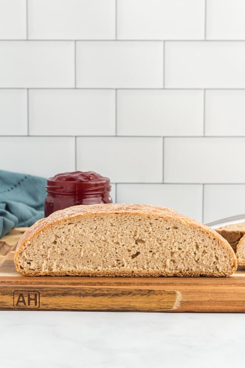 gluten free sourdough bread on a wooden cutting board with jam in the background