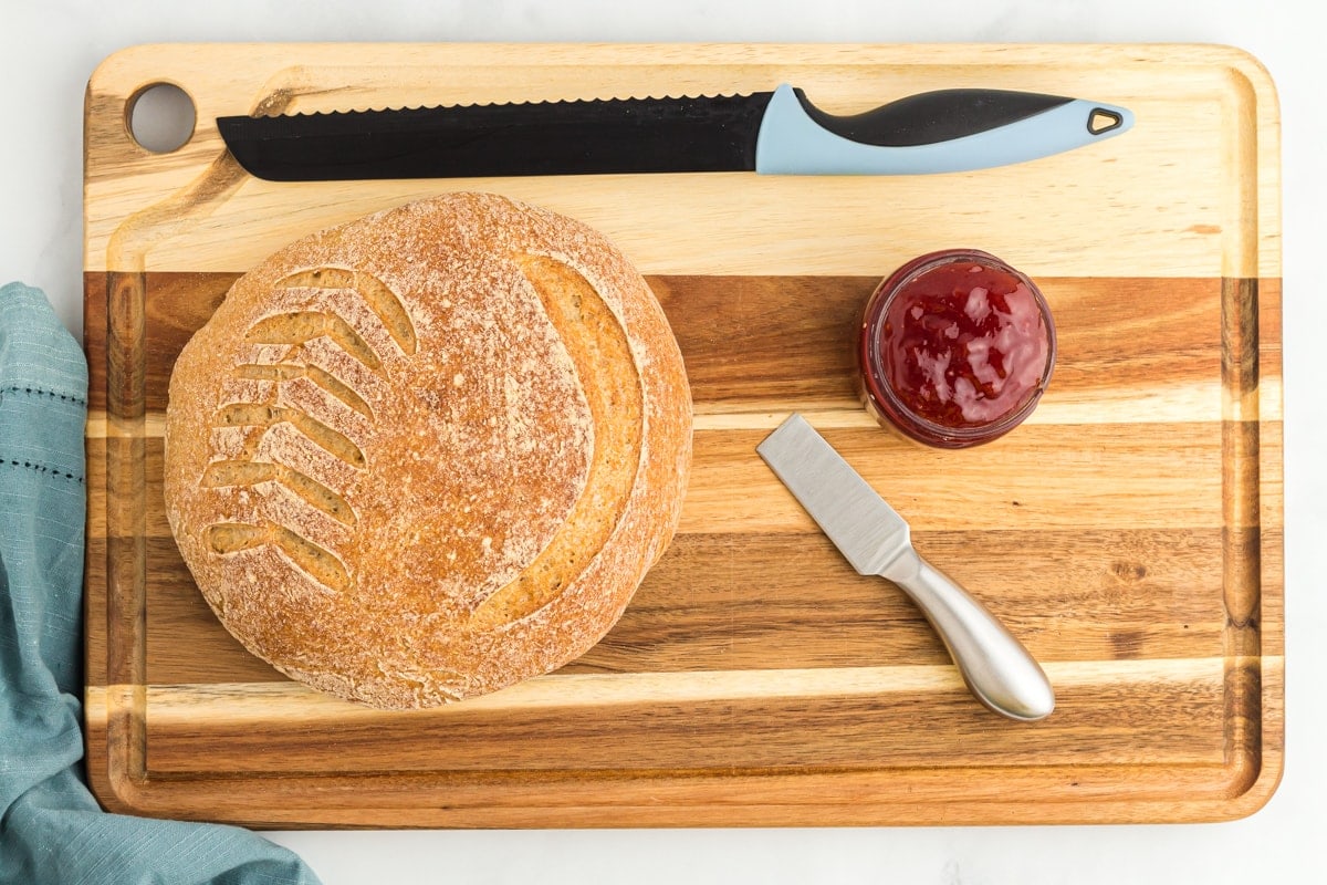 gluten free sourdough bread boule on a wooden cutting board with a knife and jam