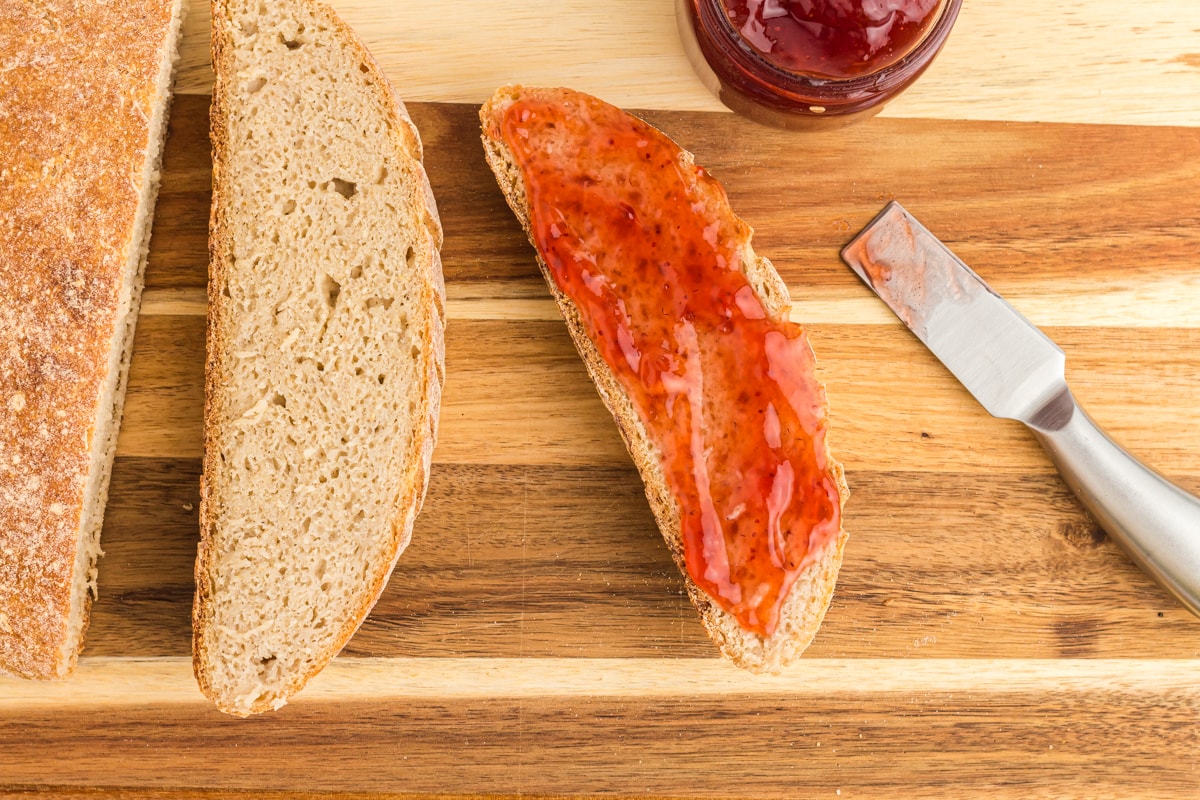 slices of gluten free sourdough bread on a wooden cutting board with a knife and jam