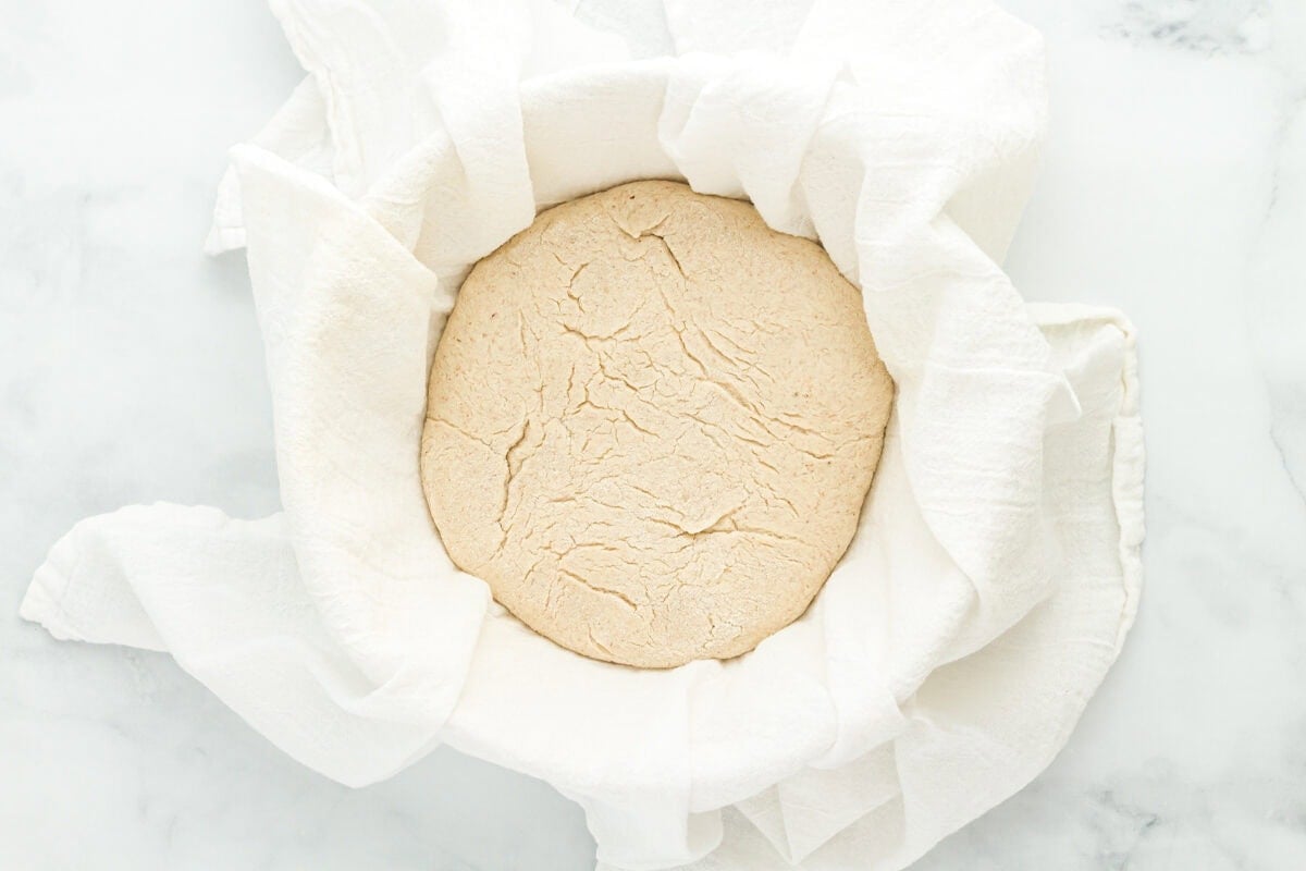 risen gluten-free sourdough bread dough in a bowl lined with cloth.