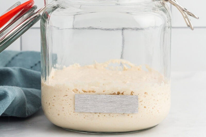 gluten free sourdough starter in a glass jar with tape on the side.