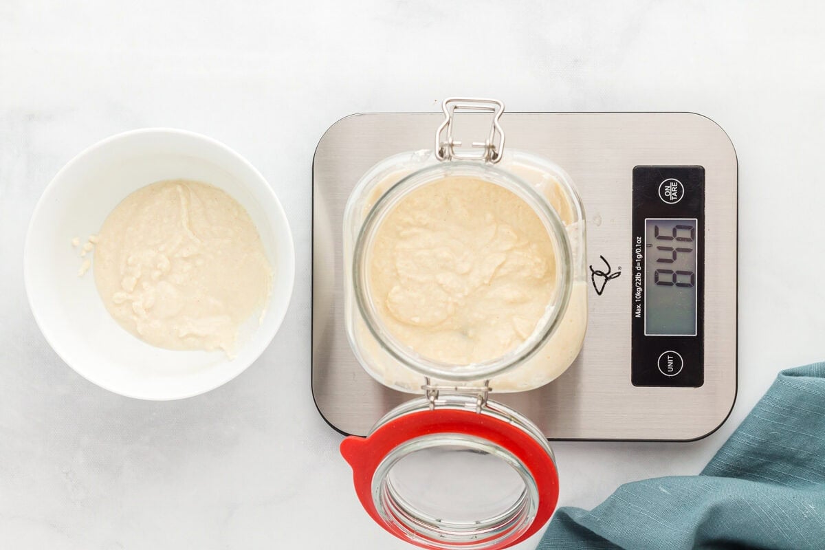 overhead view of flour, water, and gluten free sourdough starter in a glass jar on a scale.
