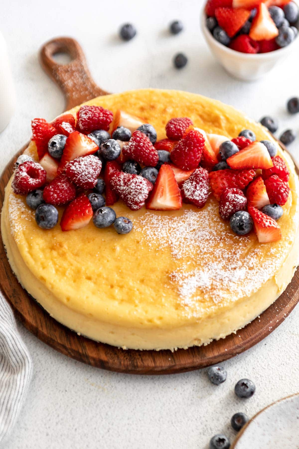 crustless cheesecake on a cake board topped with fruit and powdered sugar.