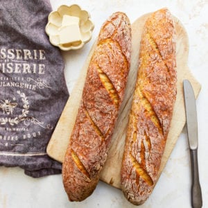 overhead view of 2 gluten free baguettes on a wooden cutting board with butter.