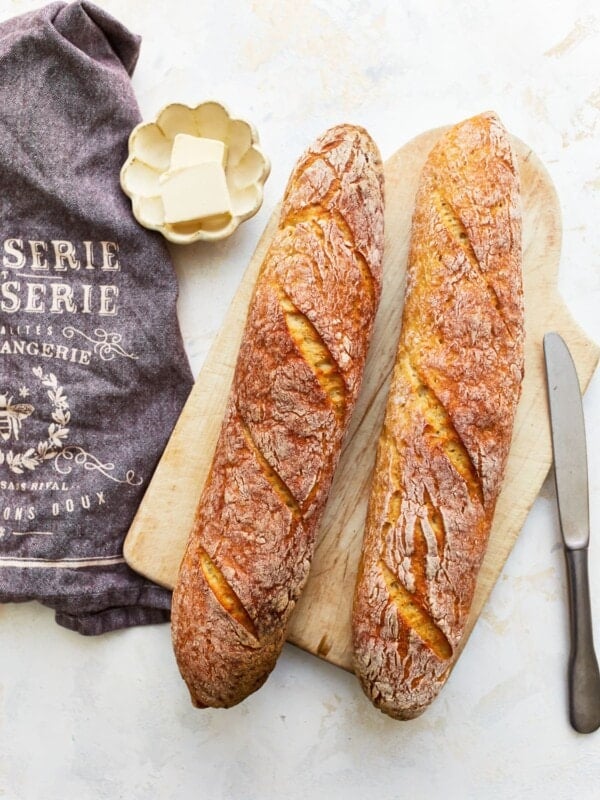 overhead view of 2 gluten free baguettes on a wooden cutting board with butter.