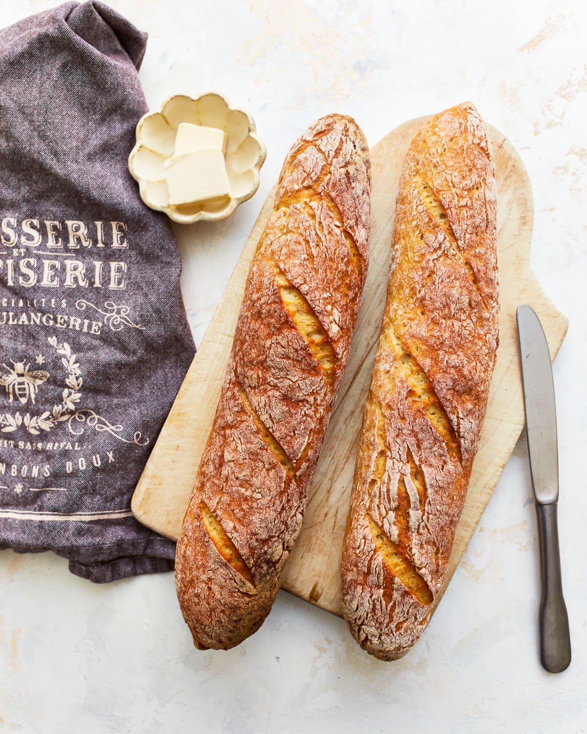 overhead view of 2 gluten free baguettes on a wooden cutting board with butter.