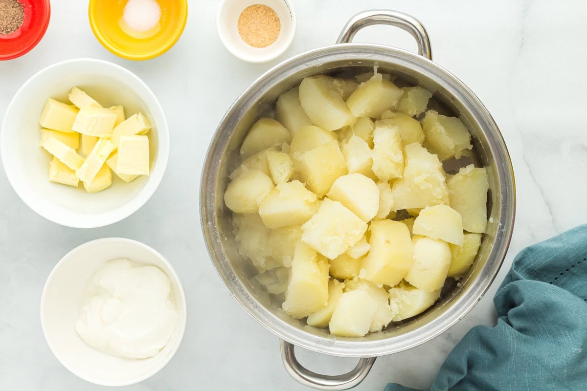 Cooked potatoes with a bowl of butter and a bowl of sour cream next to the pot.