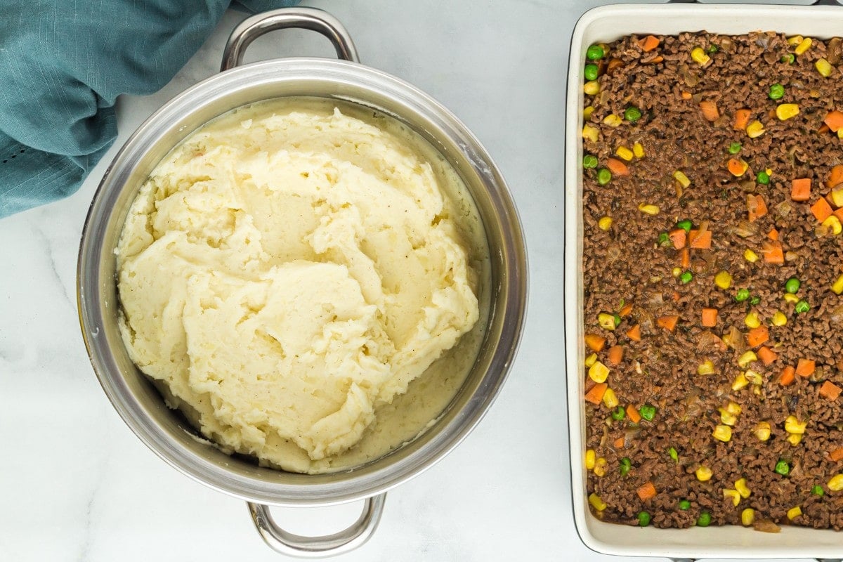 Seasoned mashed potatoes in a pot next to the baking dish of the ground beef mixture.