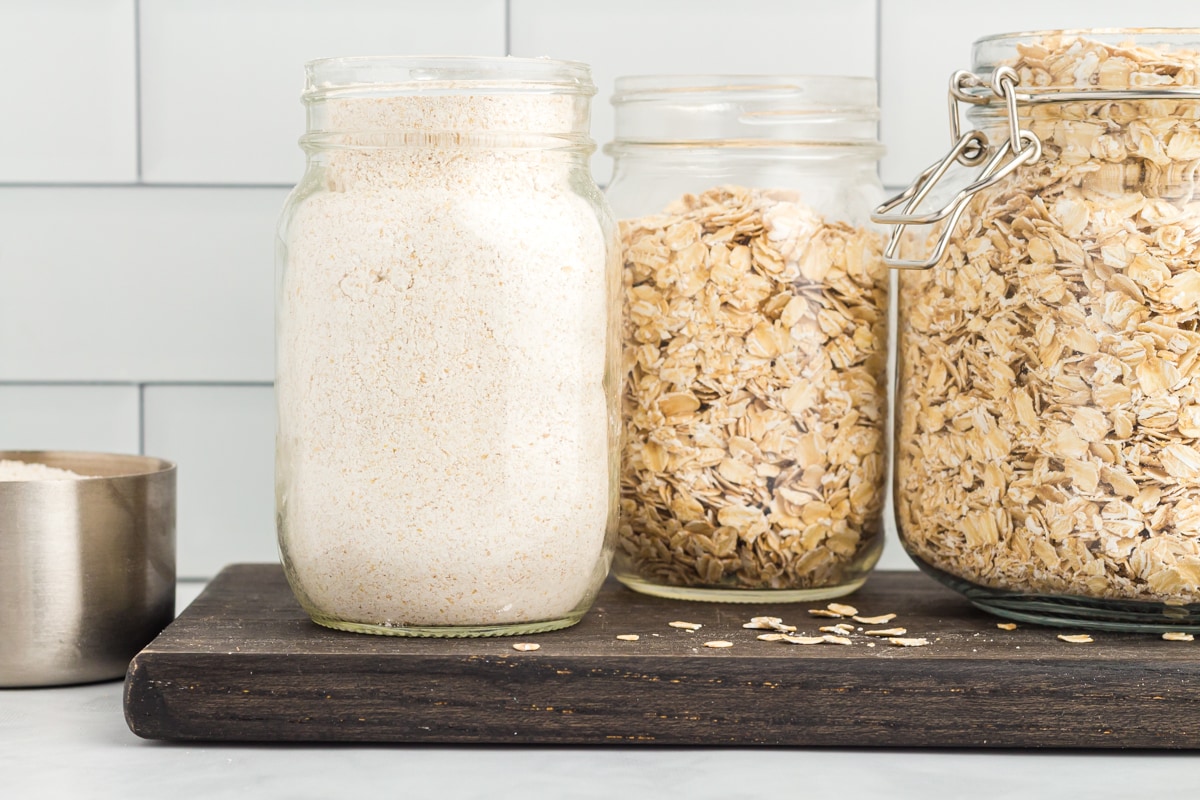 side view of oat flour in a glass jar on a wooden cutting board.