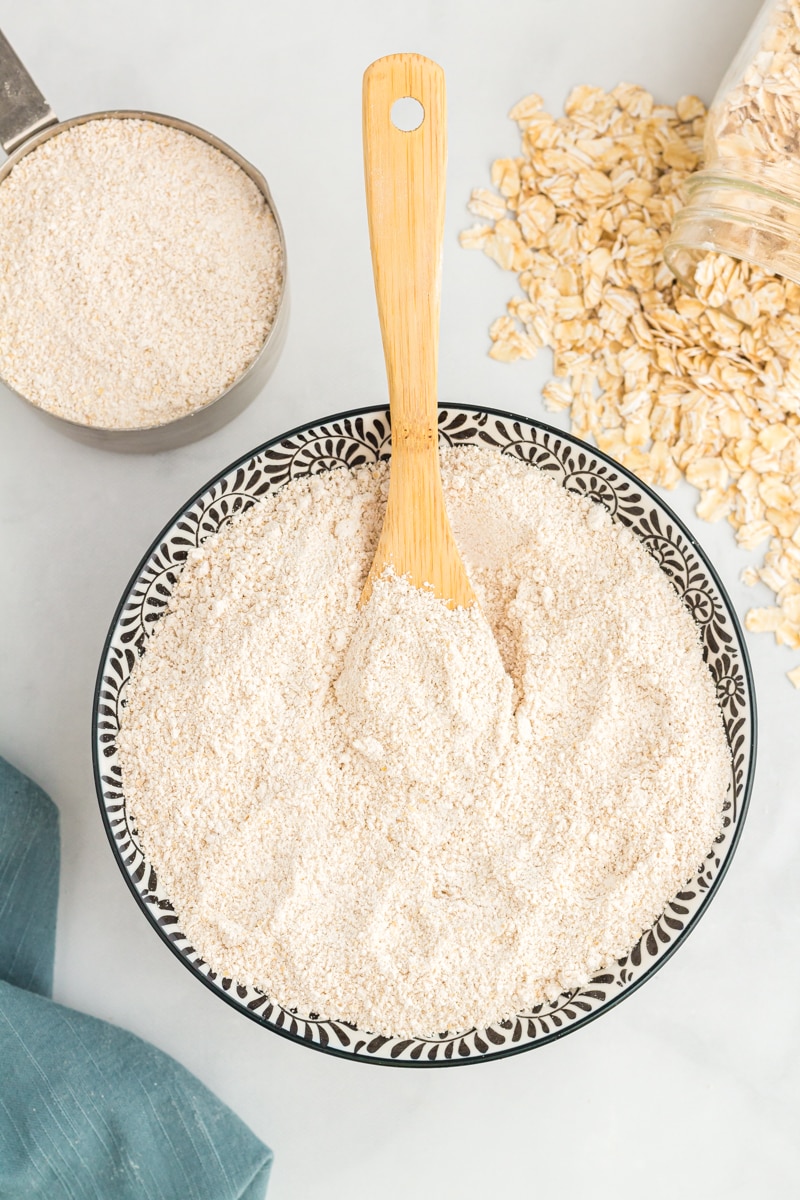 overhead view of oat flour in a decorative serving bowl with a wooden spoon.