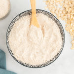overhead view of oat flour in a decorative serving bowl with a wooden spoon.