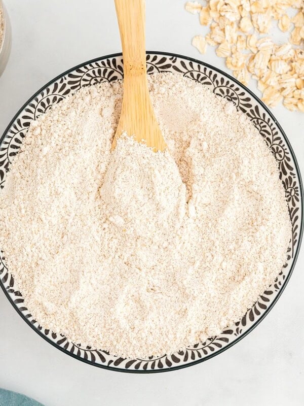 overhead view of oat flour in a decorative serving bowl with a wooden spoon.